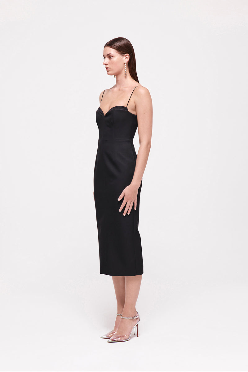 Side on image of model wearing the Bodie Dress in Black which features a sweetheart neckline and thin strap falling to a mid length silhouette.