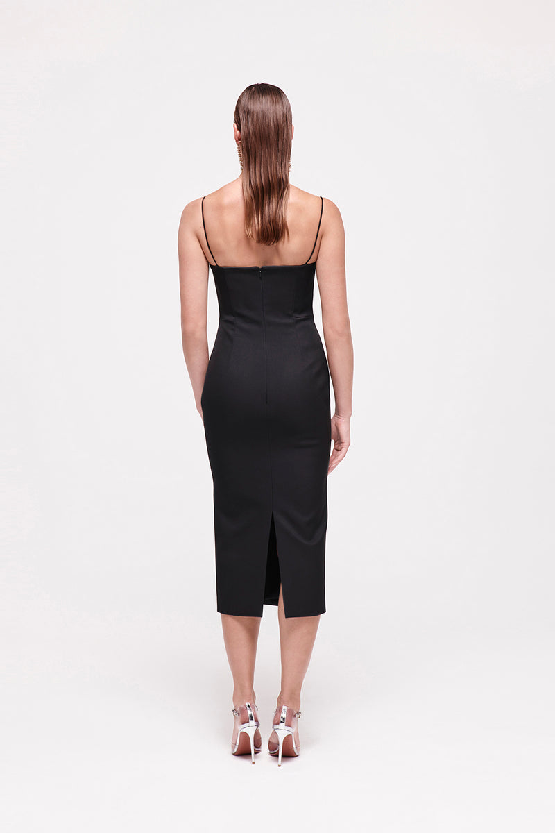 Back image of model wearing the Bodie Dress in Black which features an invisible zip and thin strap, falling to a mid length silhouette.